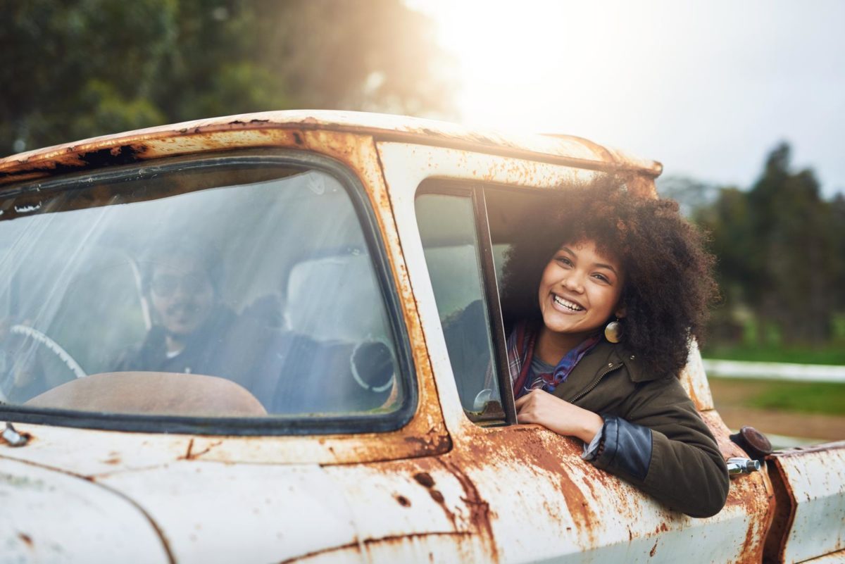 Shot of a happy young woman driving in a rusty rat rod.